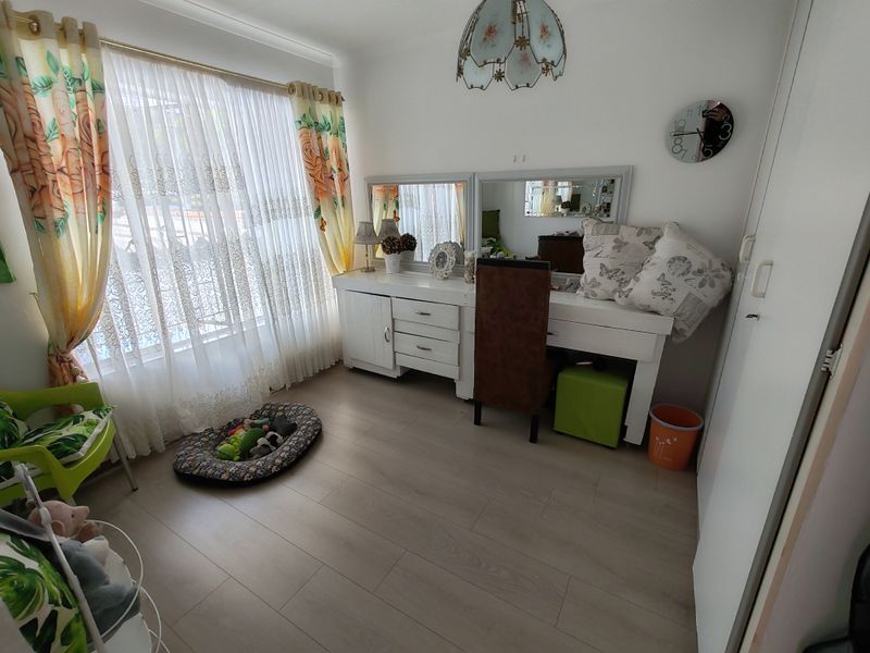 A bedroom featuring light-toned laminate flooring, a built-in wardrobe, and large windows with sheer curtains, offering a bright and functional living space.