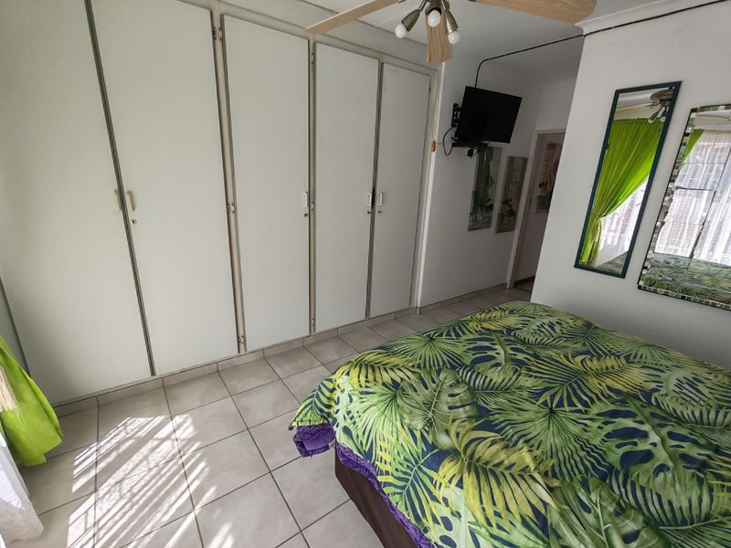 A bedroom featuring tiled flooring, built-in cupboards, and a ceiling fan, offering a functional space with neutral finishes.