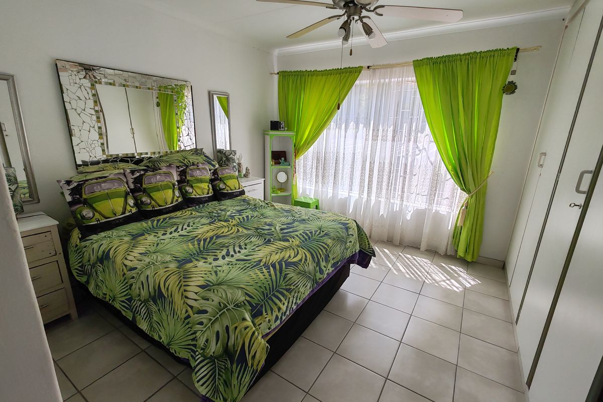 A bedroom featuring tiled flooring, a ceiling fan, and built-in cupboards, offering a functional space with natural light.
