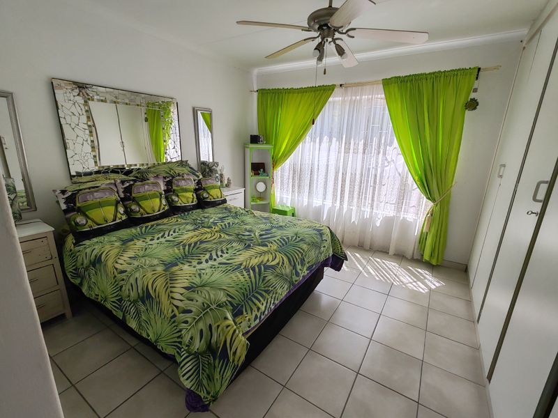 A bedroom featuring tiled flooring, a ceiling fan, and built-in cupboards, offering a functional space with natural light.
