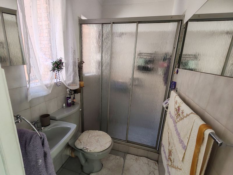 A compact bathroom featuring a shower enclosure with sliding doors, a pedestal basin, and a toilet, finished with tiled walls and flooring.