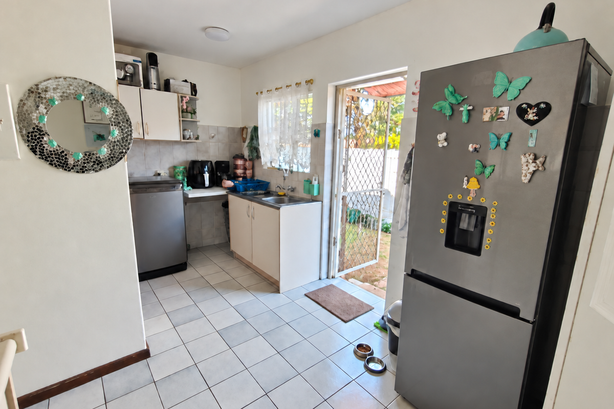Functional kitchen area featuring tiled flooring, built-in cabinetry, and direct access to the rear exterior through a security gate.