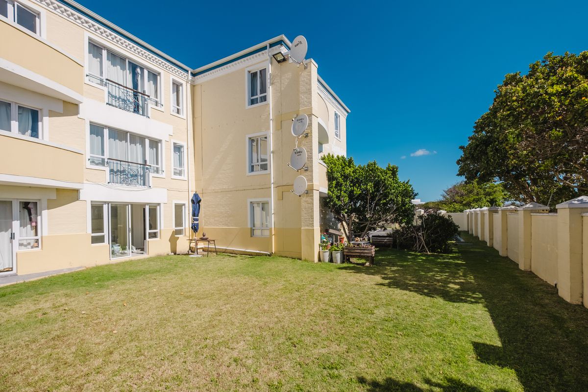 Rear view of the apartment building featuring a shared lawn area, perimeter wall, and multiple balconies with sliding door access.