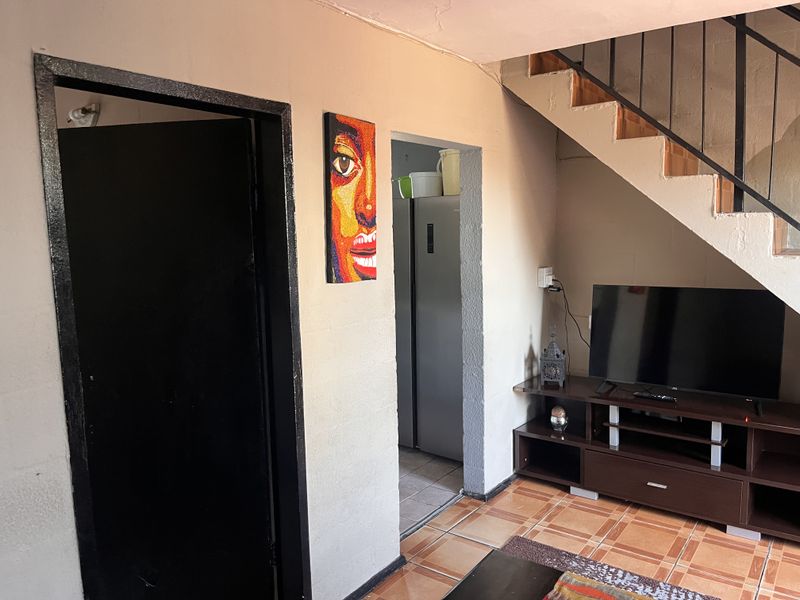 Living area featuring tiled flooring and an under-stair space with access to an adjacent room.