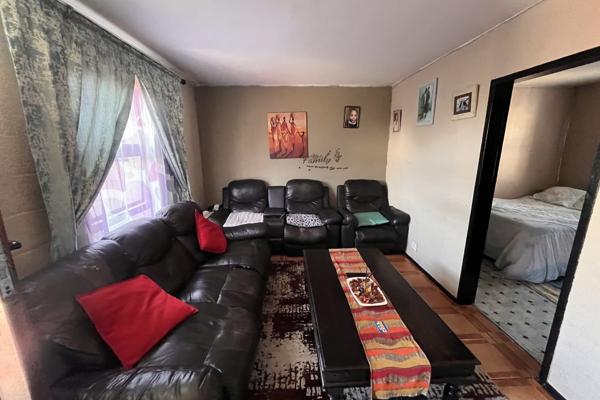 A living room featuring parquet flooring and direct access to an adjacent bedroom, showing signs of wear on the walls and ceiling.