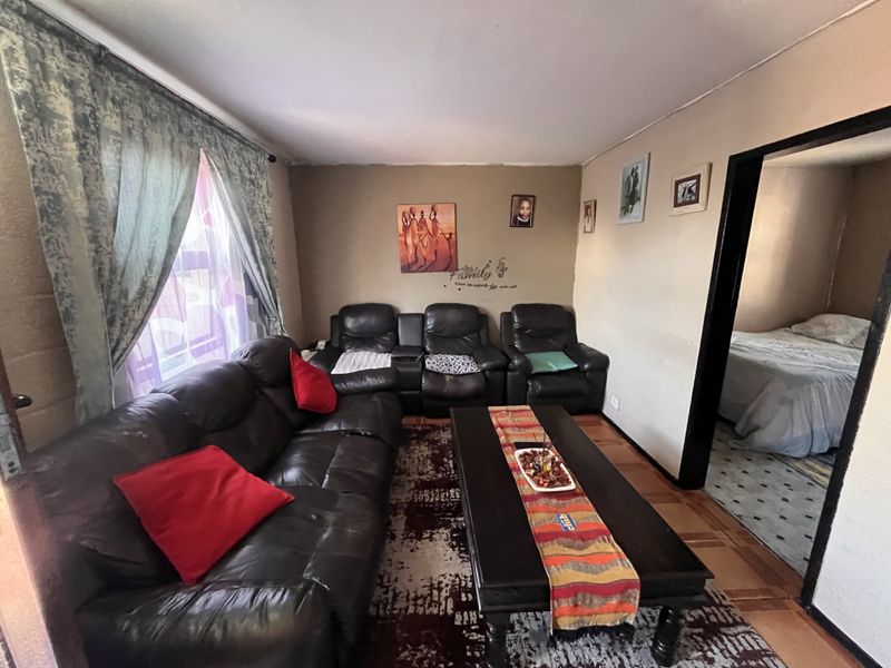 A living room featuring parquet flooring and direct access to an adjacent bedroom, showing signs of wear on the walls and ceiling.
