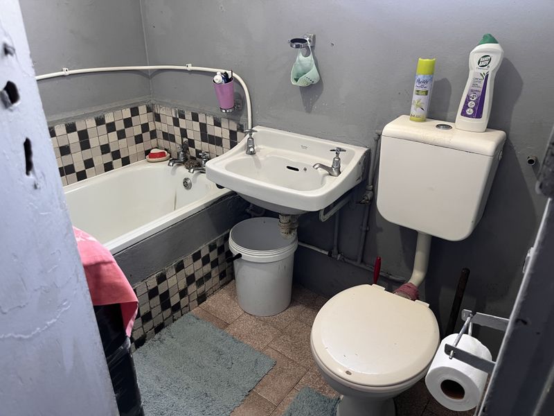 A compact bathroom featuring a standard bathtub, wall-mounted basin, and toilet with dated finishes and exposed plumbing.