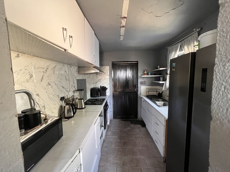 Galley-style kitchen featuring built-in cabinetry, marble-effect backsplash, and integrated appliances. The space requires ceiling and flooring repairs to improve overall condition.