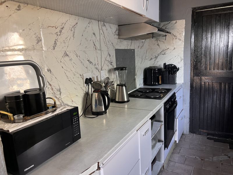 A functional kitchen featuring a marble-effect tiled backsplash, built-in oven, electric hob, and extractor fan with fitted cabinetry.