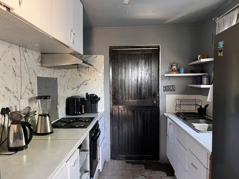 Compact kitchen featuring white cabinetry, marble-look splashback, built-in oven and hob, and a functional sink area with floating shelving.