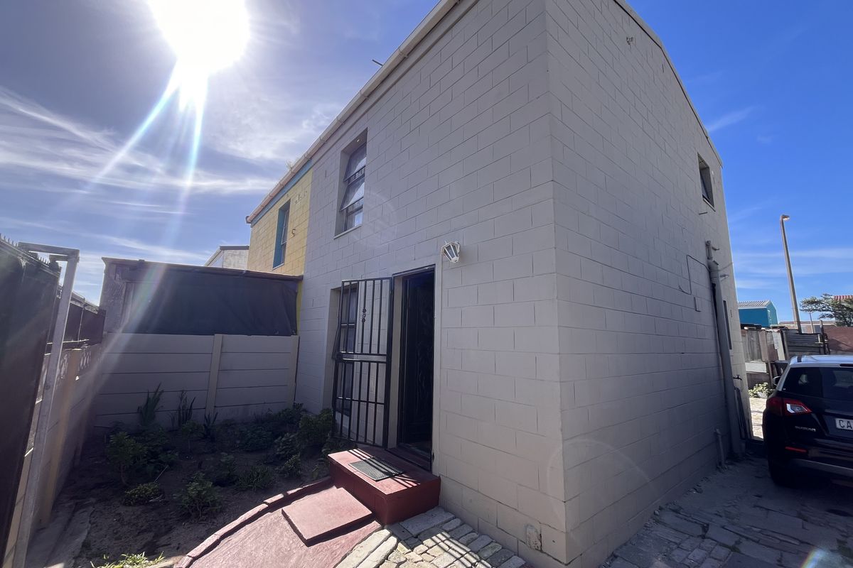 Rear exterior view of the property featuring a concrete block facade, security gate, paved walkway, and a small garden area.