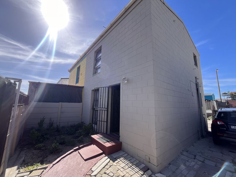 Rear exterior view of the property featuring a concrete block facade, security gate, paved walkway, and a small garden area.
