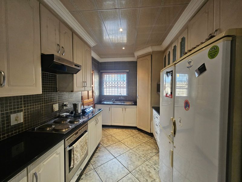 A functional kitchen featuring built-in cabinetry, granite countertops, an electric hob with extractor, and tiled finishes throughout.