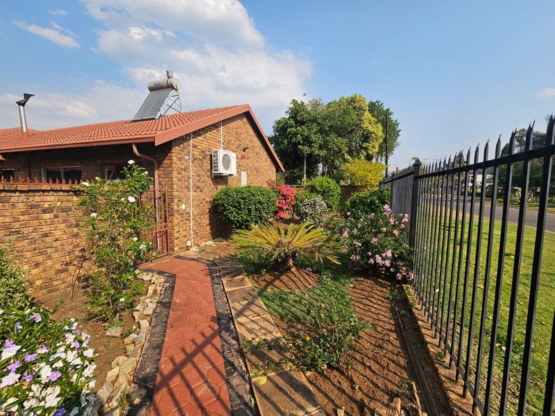 A well-maintained face brick home exterior featuring a solar water heater, air conditioning unit, paved walkway, and secure metal perimeter fencing.