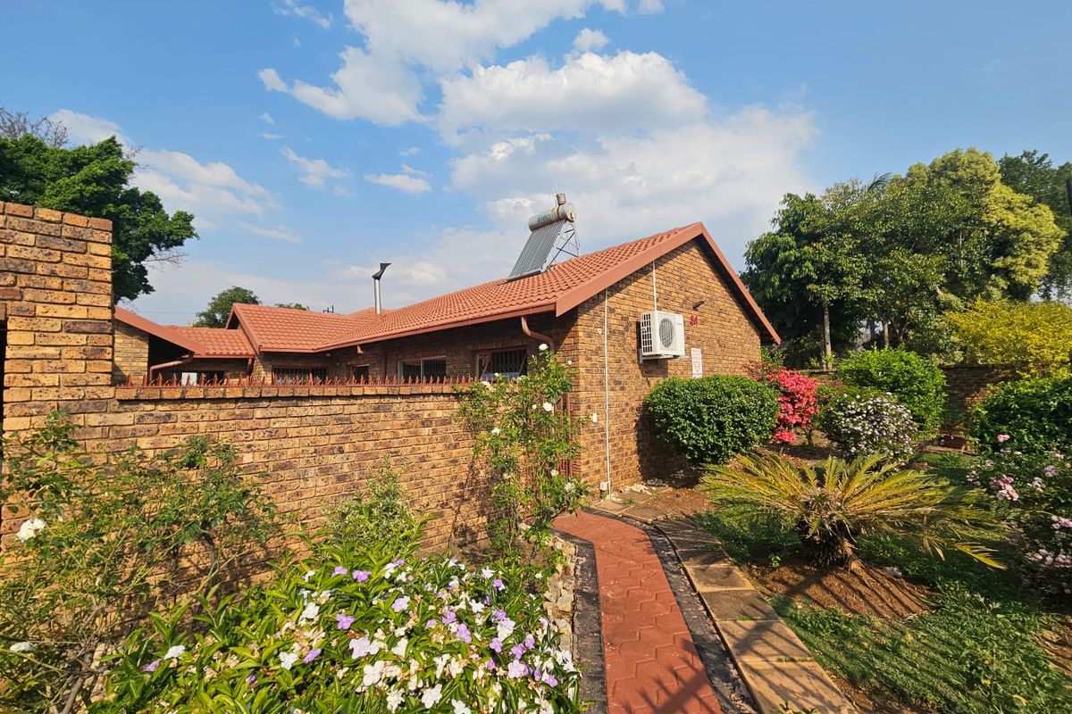 A well-maintained face brick exterior featuring a tiled roof, solar water heating system, and a paved garden walkway.