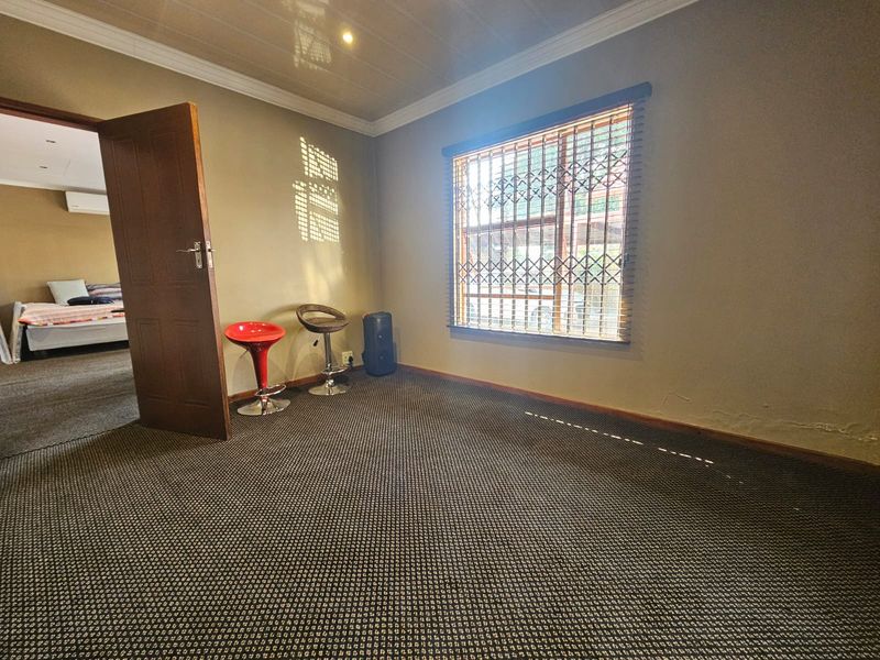 A spacious bedroom featuring carpeted flooring, a security gate on the window, and coved ceilings, showing signs of wall dampness and wear.