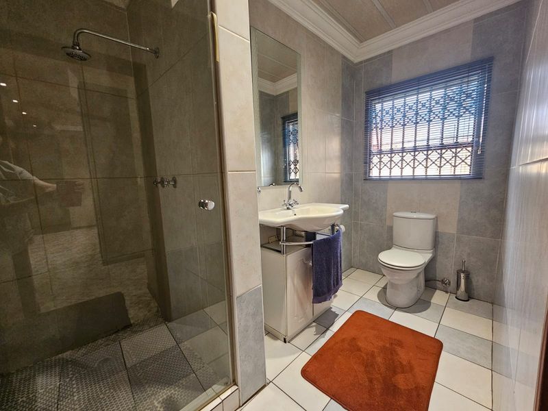 A functional bathroom featuring a glass-enclosed shower, vanity basin, and toilet, finished with neutral wall and floor tiling.