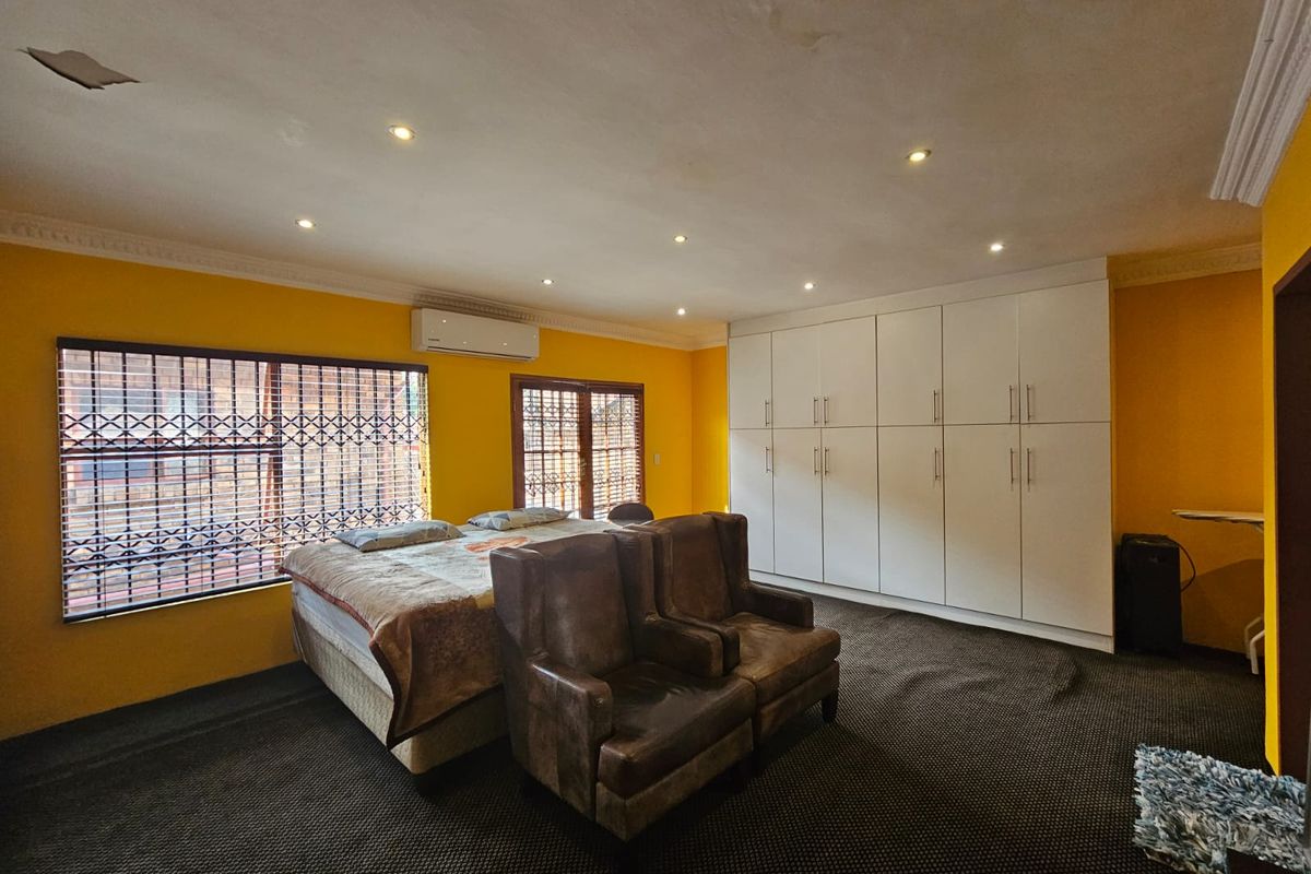 Spacious bedroom featuring extensive built-in cupboards, recessed lighting, and an air conditioning unit, with yellow walls and dark carpeting.