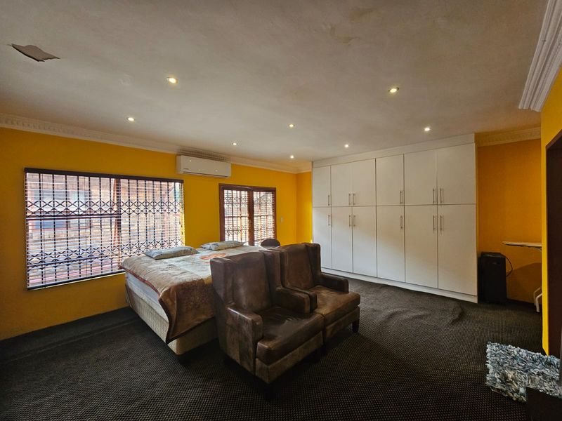 Spacious bedroom featuring extensive built-in cupboards, recessed lighting, and an air conditioning unit, with yellow walls and dark carpeting.