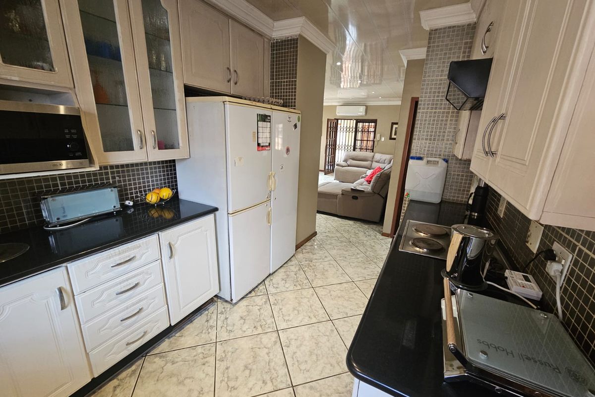 A functional kitchen featuring white cabinetry, black granite countertops, mosaic tile backsplashes, and ceramic floor tiles, with an open flow into the adjacent living area.