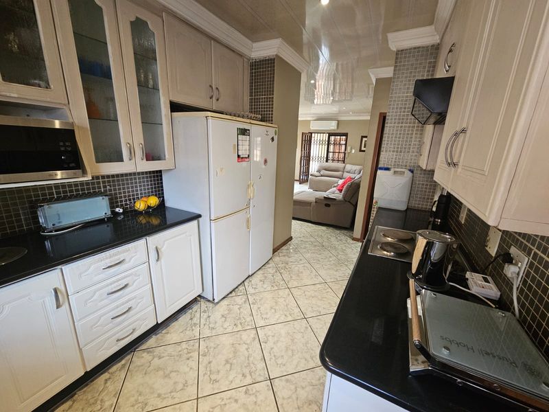 A functional kitchen featuring white cabinetry, black granite countertops, mosaic tile backsplashes, and ceramic floor tiles, with an open flow into the adjacent living area.