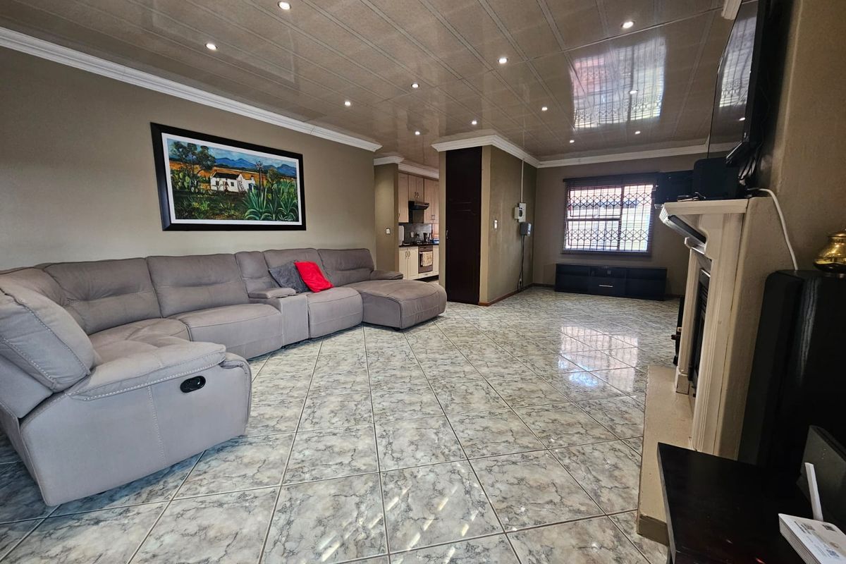 Spacious living room featuring tiled flooring, recessed downlighting, and a fireplace, with an open flow towards the kitchen area.