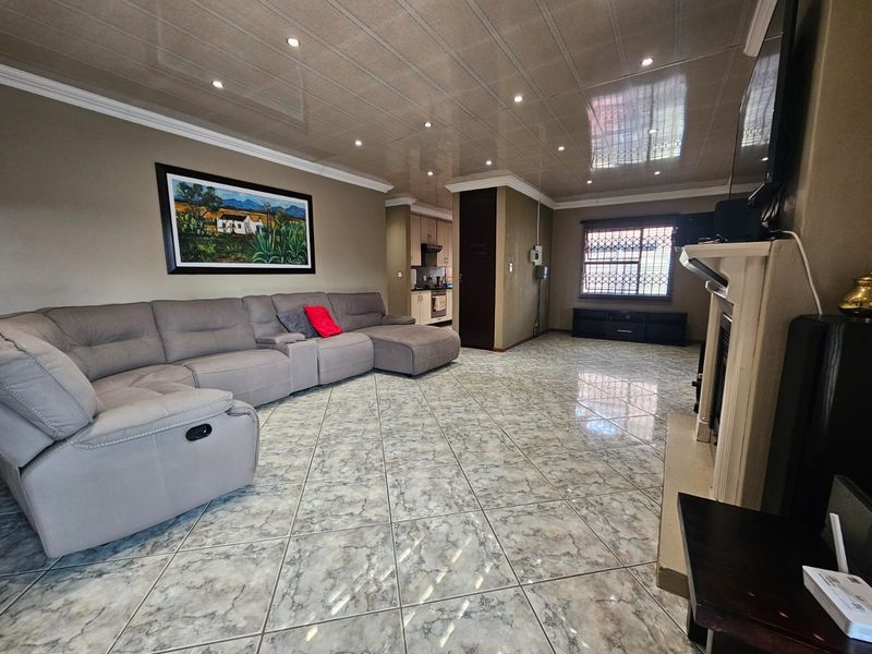 Spacious living room featuring tiled flooring, recessed downlighting, and a fireplace, with an open flow towards the kitchen area.