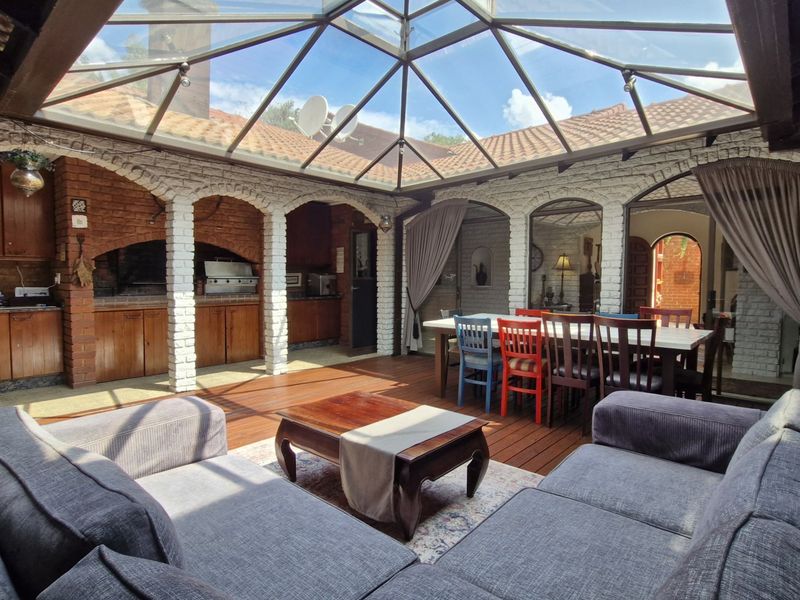 Spacious enclosed patio featuring a glass roof, exposed brick arches, and a built-in braai area, perfect for year-round outdoor entertaining.