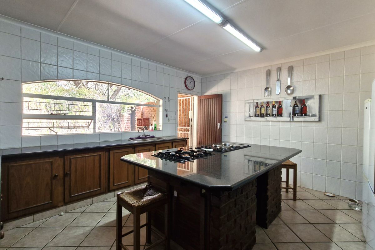 Spacious kitchen featuring a large central island with a gas hob, granite countertops, ample wooden cabinetry, and a large arched window.
