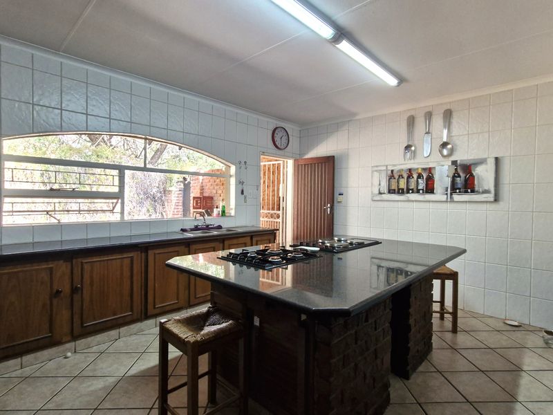 Spacious kitchen featuring a large central island with a gas hob, granite countertops, ample wooden cabinetry, and a large arched window.