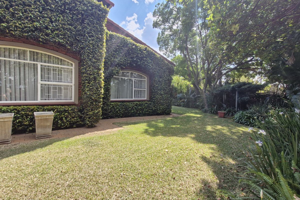 A well-maintained rear garden featuring a lush ivy-covered brick facade, arched windows, and established landscaping with paved walkways.