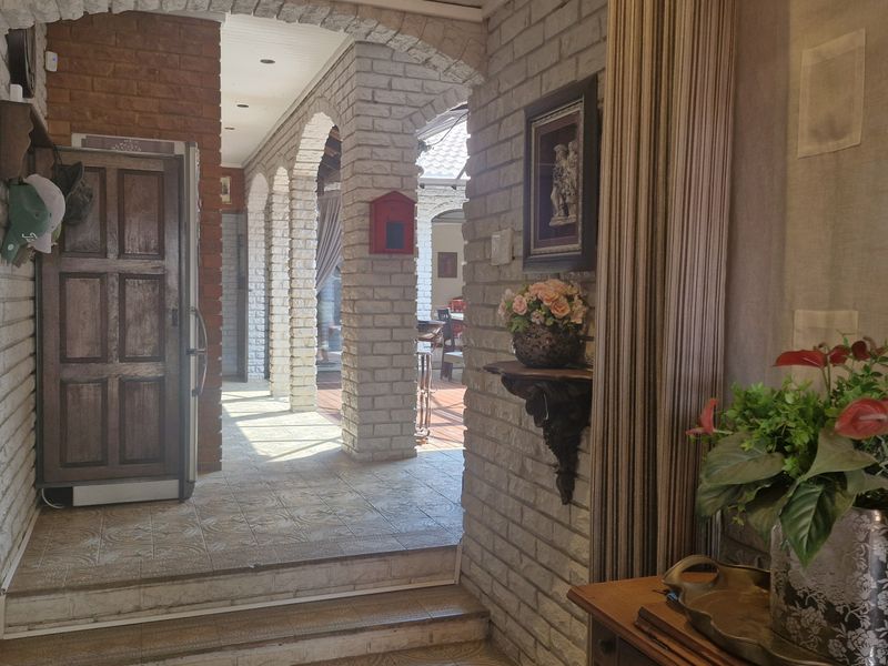 An inviting entryway featuring rustic exposed brick walls, decorative archways, and tiled flooring, leading through to an outdoor patio area.