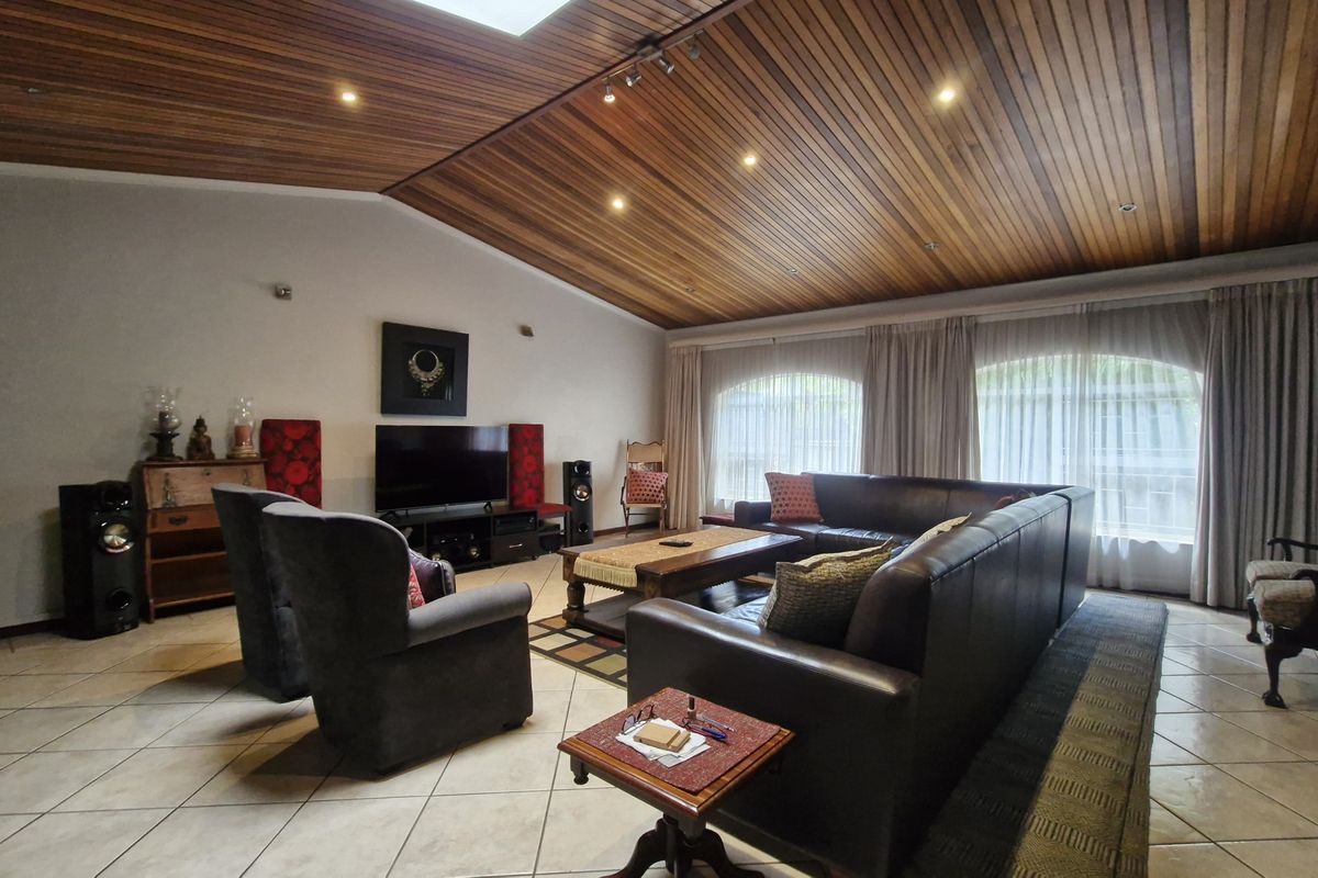 Spacious living room featuring a distinctive timber-clad vaulted ceiling, tiled flooring, and large arched windows that provide ample natural light.