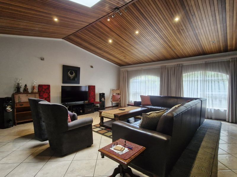 Spacious living room featuring a distinctive timber-clad vaulted ceiling, tiled flooring, and large arched windows that provide ample natural light.