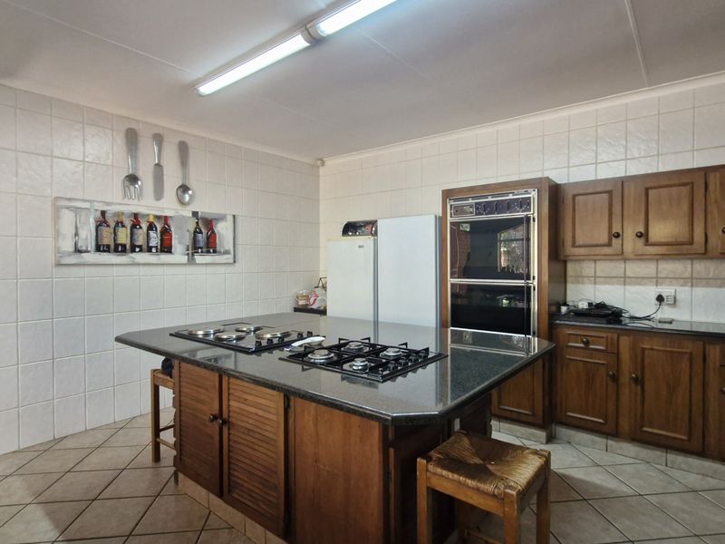 Spacious kitchen featuring wooden cabinetry, granite countertops, a central island with a built-in gas hob, and a double oven.