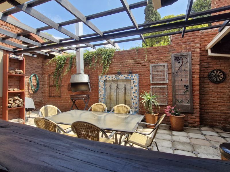 Covered outdoor patio featuring a timber pergola, exposed brick walls, and a built-in braai, perfect for alfresco dining and entertaining.