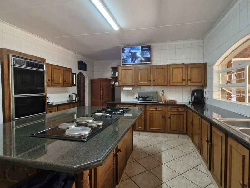 Spacious kitchen featuring extensive wooden cabinetry, granite countertops, a central island with a gas hob, and a double eye-level oven.