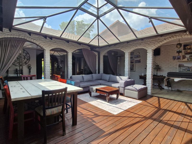 Spacious covered patio featuring a large glass skylight roof, timber decking, and charming exposed brick arches, perfect for outdoor entertaining.