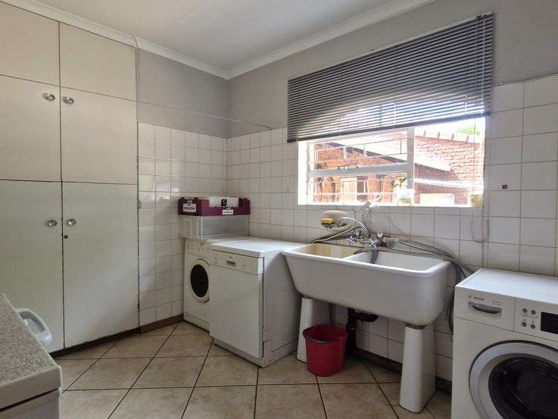 Functional laundry room featuring built-in storage cabinetry, a double ceramic wash trough, tiled splashbacks, and tiled flooring.
