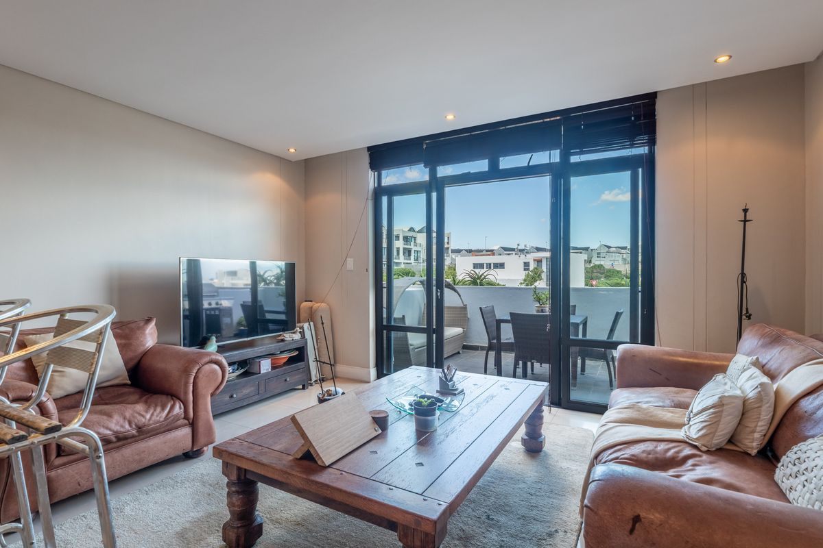A bright living room featuring tiled floors, recessed lighting, and large sliding glass doors that open onto a private balcony.