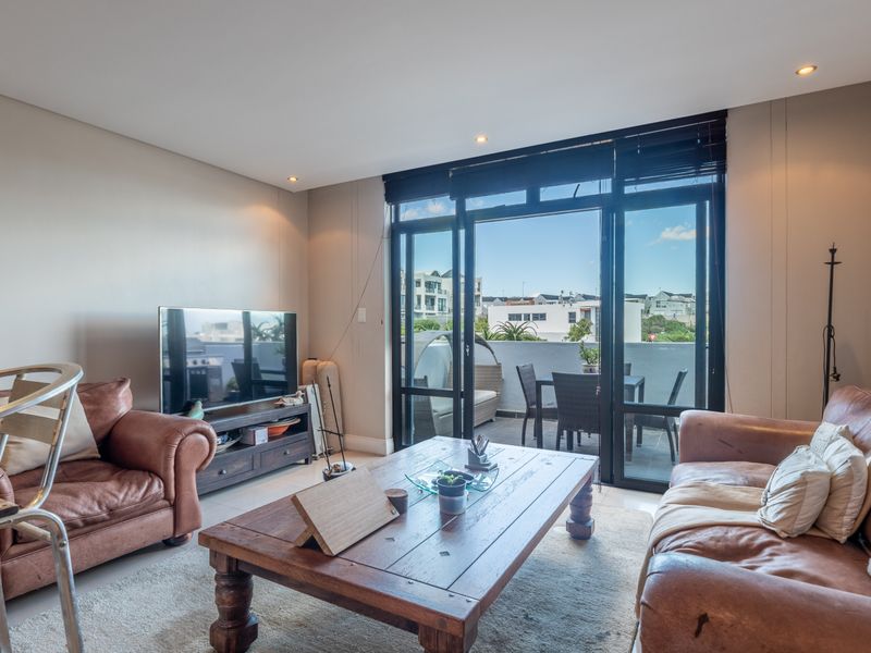 A bright living room featuring tiled floors, recessed lighting, and large sliding glass doors that open onto a private balcony.