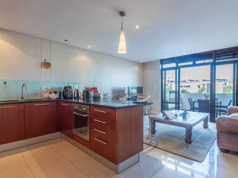 Open-plan living area featuring a modern kitchen with wood-finish cabinetry, stone countertops, and direct access to a private balcony through sliding glass doors.