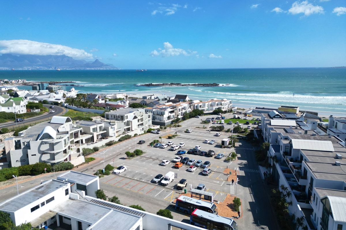 An aerial view of a coastal residential area featuring a parking lot, nearby beach, and ocean views.