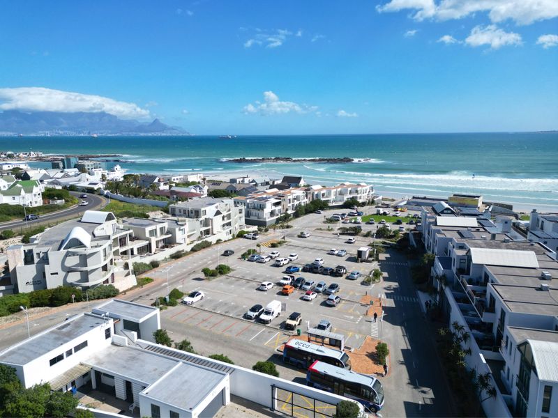 An aerial view of a coastal residential area featuring a parking lot, nearby beach, and ocean views.