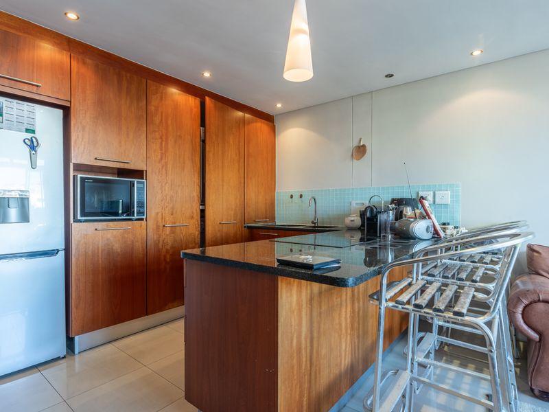 Open plan kitchen featuring warm wood cabinetry, granite countertops, a tiled backsplash, and integrated lighting, seamlessly connecting to the living area.