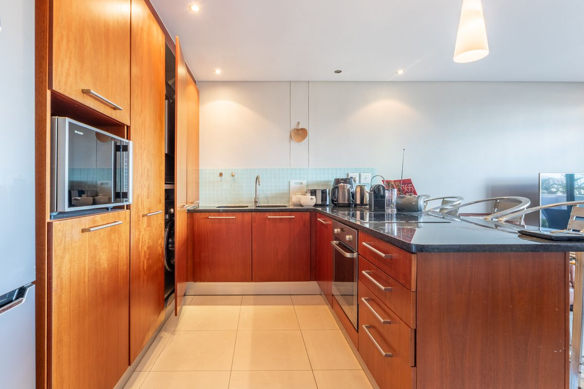 Modern kitchen featuring warm wood cabinetry, granite countertops, integrated appliances, and a tiled backsplash, offering a functional and well-maintained cooking space.