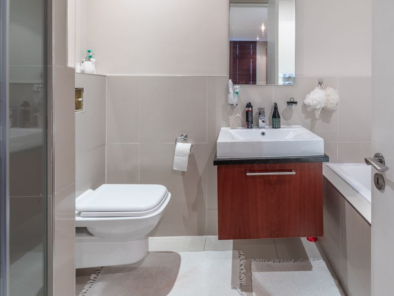 A modern bathroom featuring a wall-mounted toilet, vanity cabinet with basin, shower enclosure, and a bathtub with neutral wall tiling.