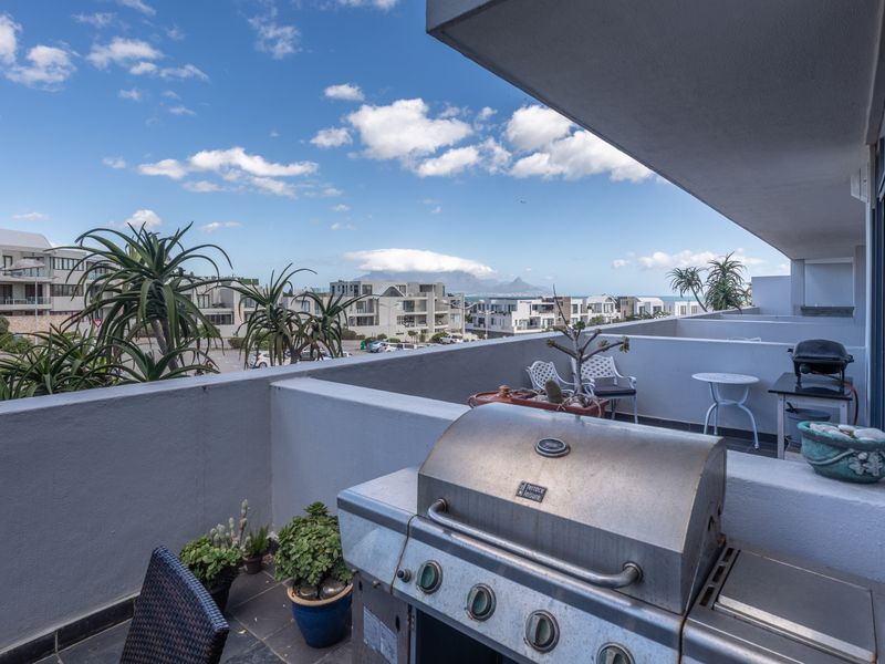 Spacious balcony featuring tiled flooring, a concrete balustrade, and an overhanging roof, offering scenic views of the surrounding neighborhood and distant mountains.