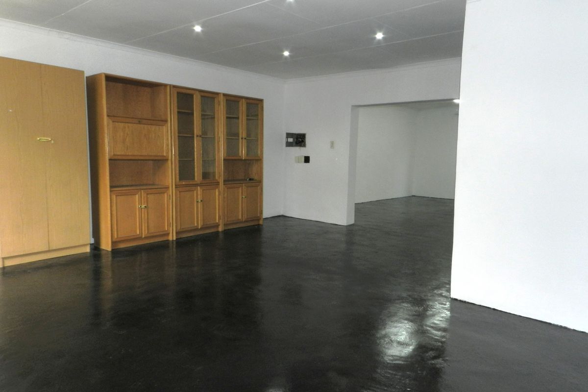 Spacious living area featuring recessed downlights, built-in wooden cabinetry, and a dark painted concrete floor, offering a blank canvas for renovation.