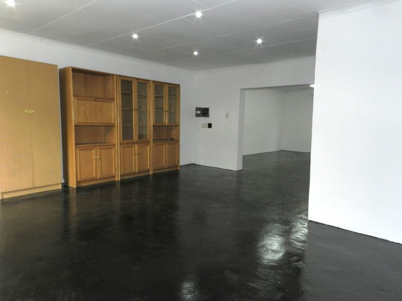 Spacious living area featuring recessed downlights, built-in wooden cabinetry, and a dark painted concrete floor, offering a blank canvas for renovation.